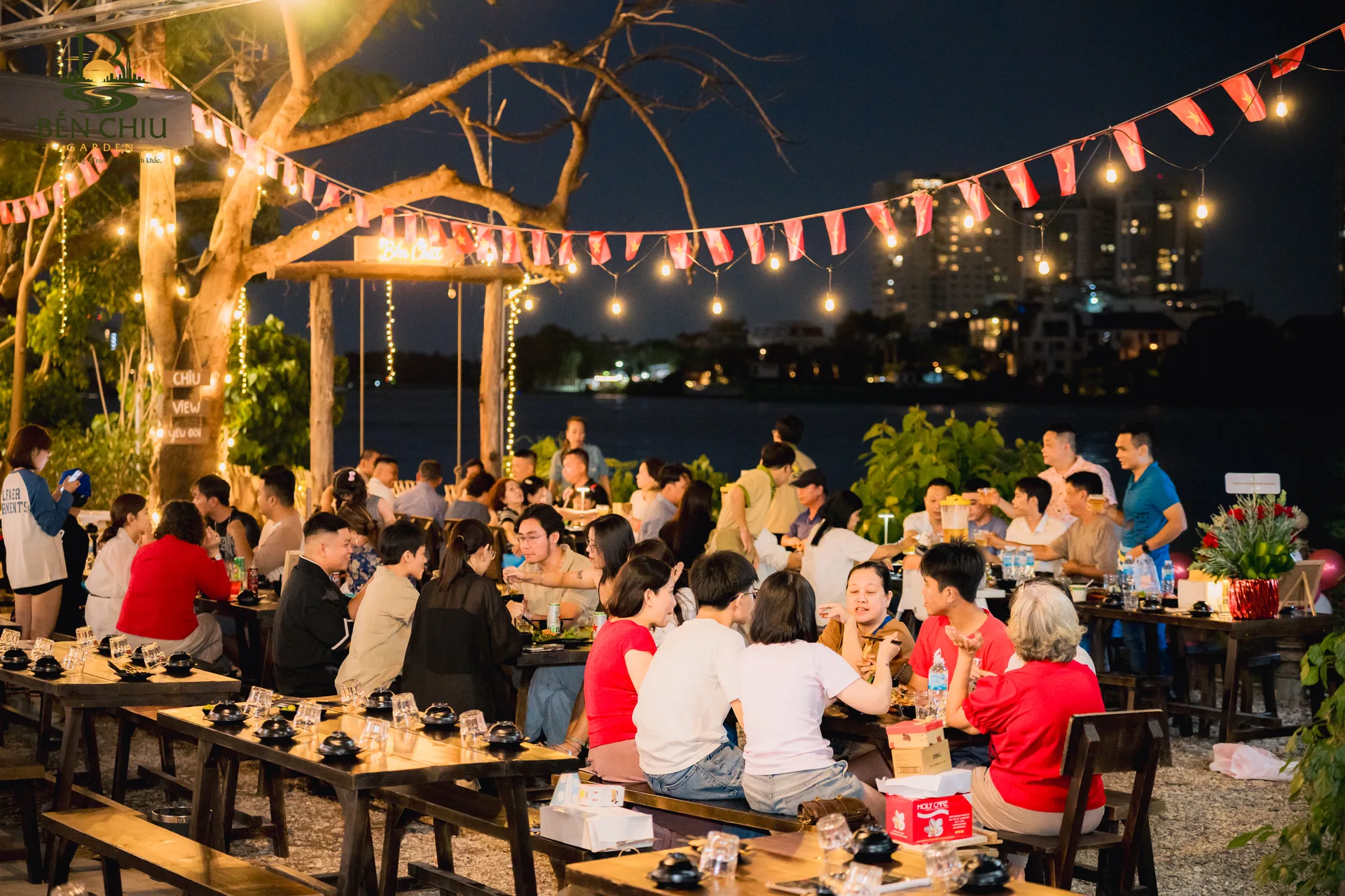 Sân vườn ven sông rực sáng dưới dây đèn buổi tối